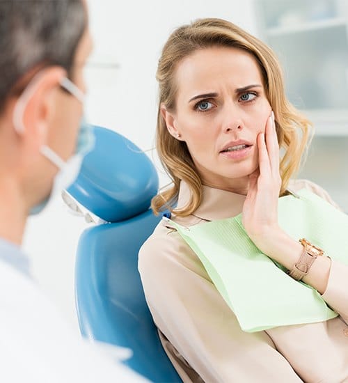 Woman holding cheek during dental crown consultation