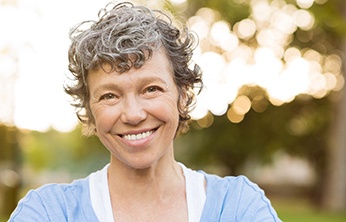Middle-aged woman smiling outside with curly grey hair