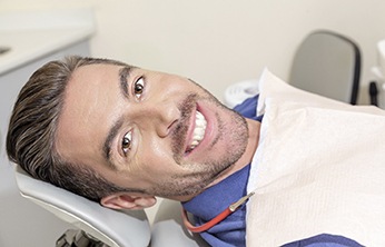 Man with a mustache smiling while sitting in dental chair