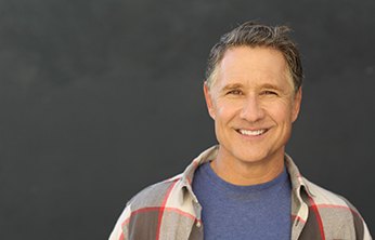 Man in flannel and greying hair smiling with dark background