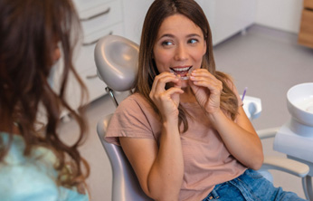 Woman sitting in dental chair putting in clear aligner