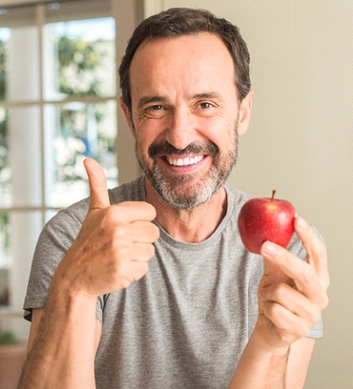 Man smiling while wearing grey shirt and holding red apple