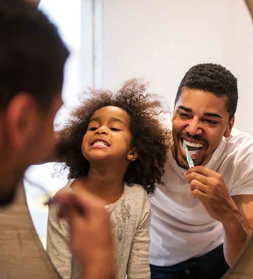 Father showing daughter how to brush teeth