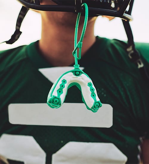 Teen with green mouthguard attached to football helmet