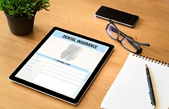 Dental insurance form on a tablet next to glasses, notepad, phone, and plant