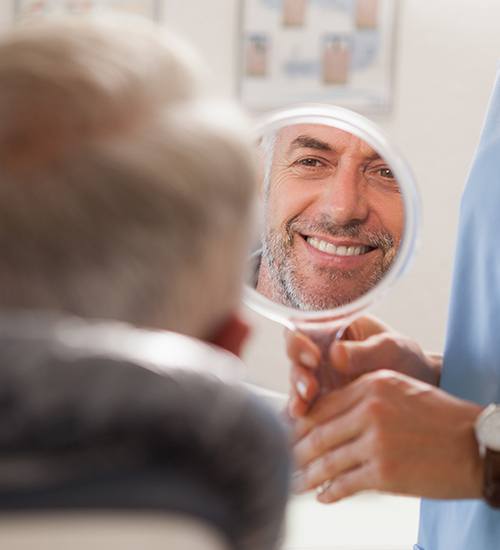 Man looking in mirror after smile makeover treatment