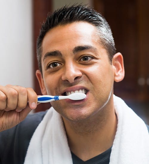 Man with a new dental crown brushing his teeth