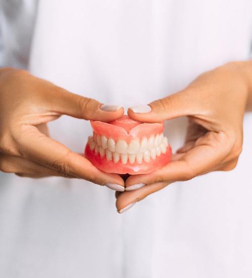 Manicured hands holding dentures for upper and lower arch