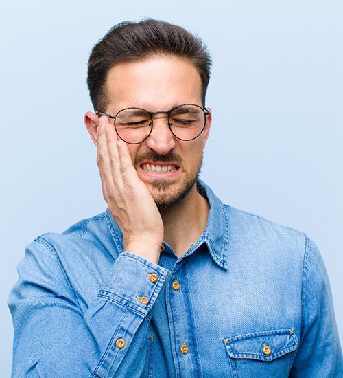 Man in blue shirt with hand on face due to dental pain