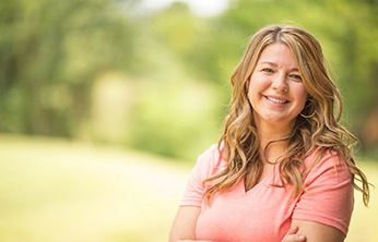 Woman in pink shirt smiling with arms crossed while outside