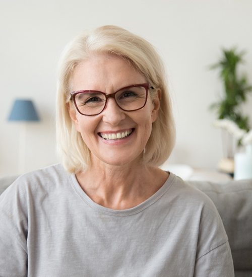 Senior woman with glasses sitting on couch and smiling