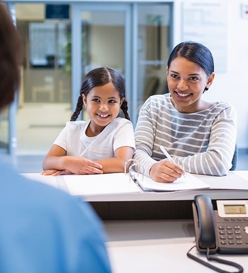 Mother and child filling out dental insurance forms at reception desk