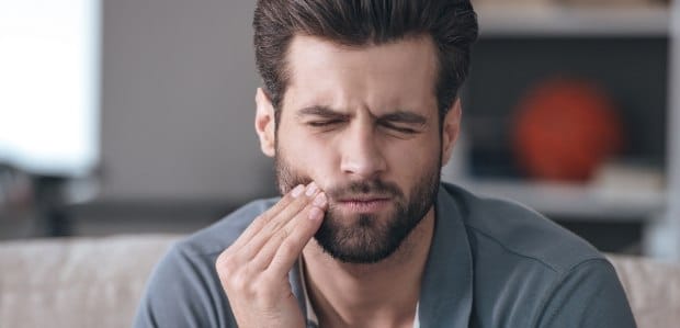 Man in need of emergency dentistry holding jaw in pain