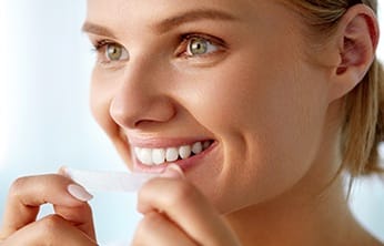 Woman using over the counter teeth whitening strips