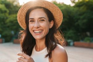 Woman who is protecting her smile while wearing a hat outside