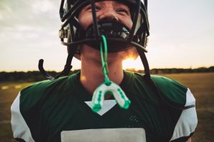 Boy playing football with mouthguard hanging from face mask