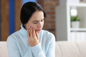 Woman with sweater sitting on couch with pain on one side of jaw
