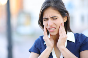 Woman in blue shirt rubbing her jaw in pain