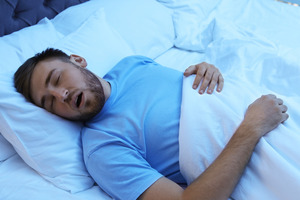 Man in blue shirt lying in bed and snoring
